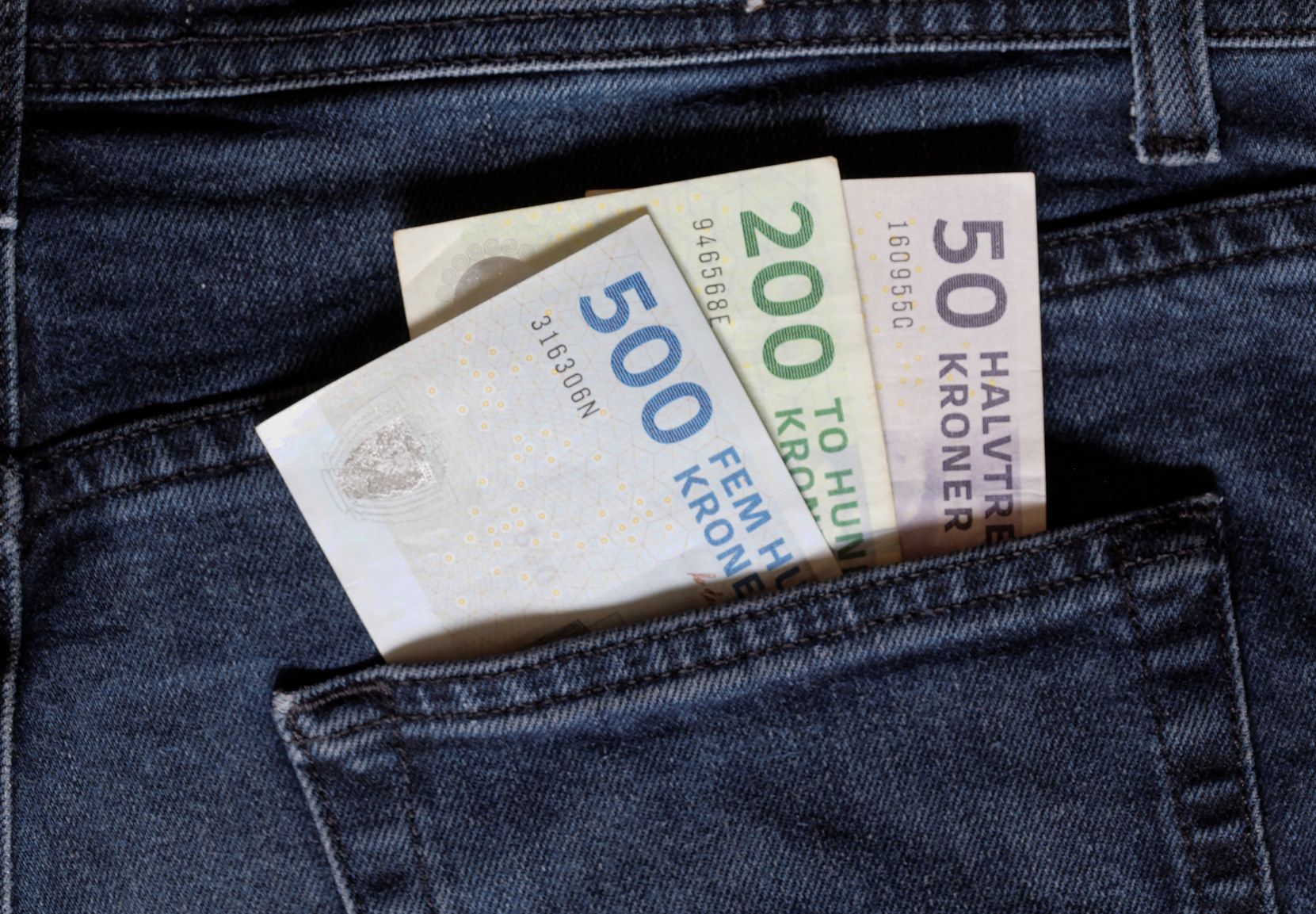 Foto af tre danske pengesedler, der stikker op af en baglomme på et par jeans
