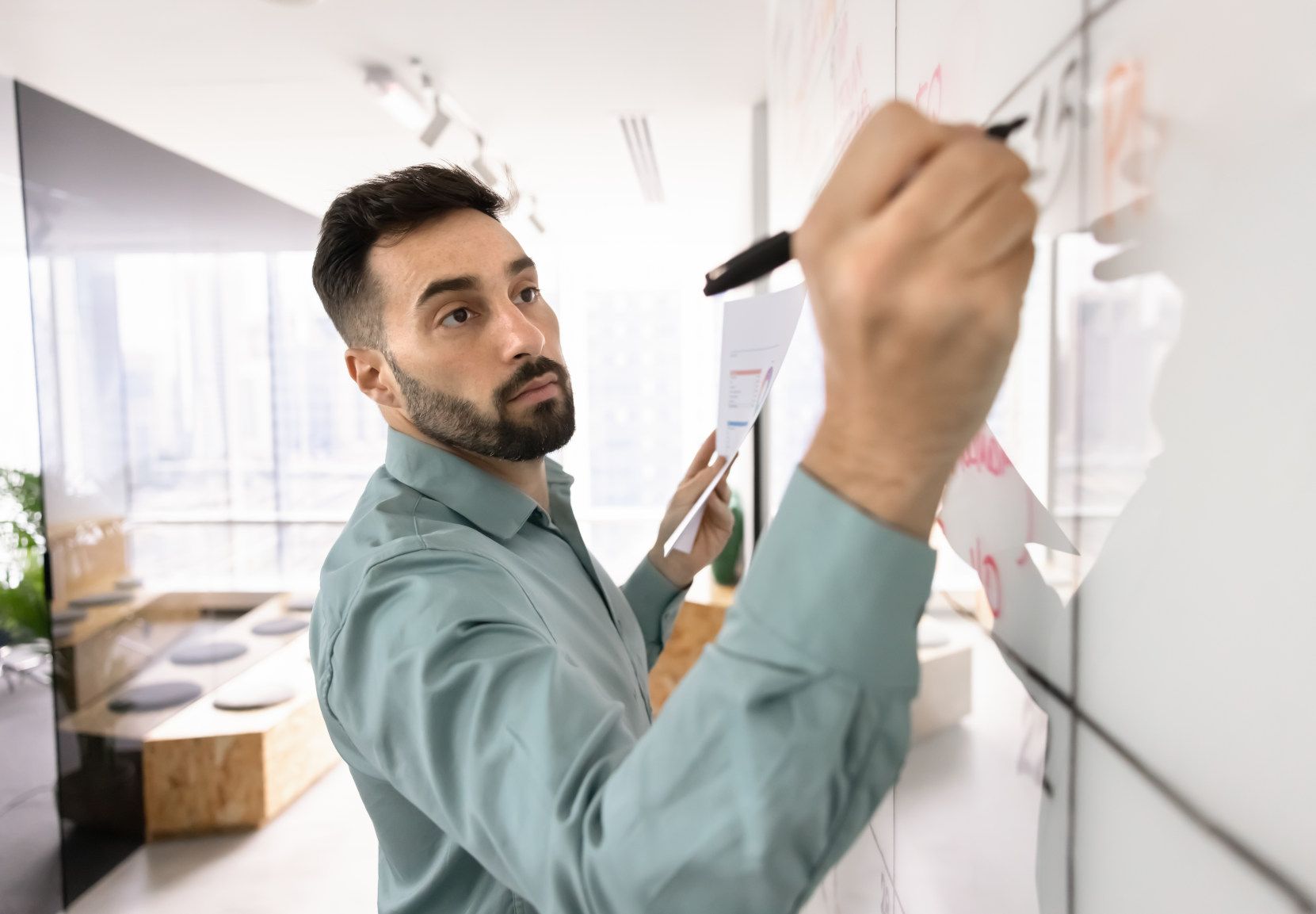 Foto af ung mand, der befinder sig i et moderne kontorlandskab og skriver på et whiteboard
