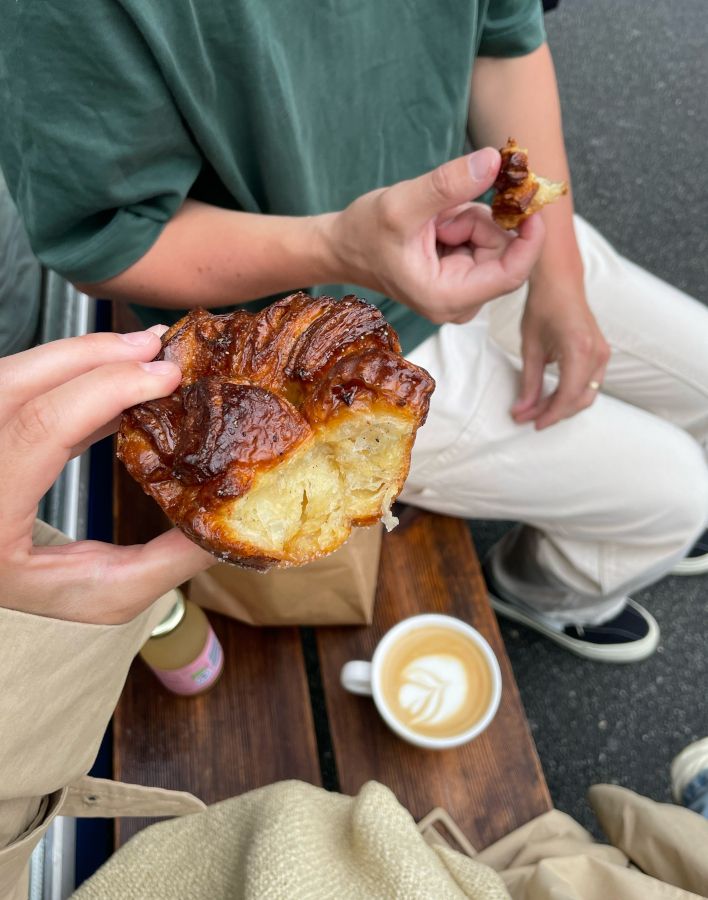Foto af to personer på en bænk, akkompagneret af en kop kaffe og noget, der ligner dyrt bagværk