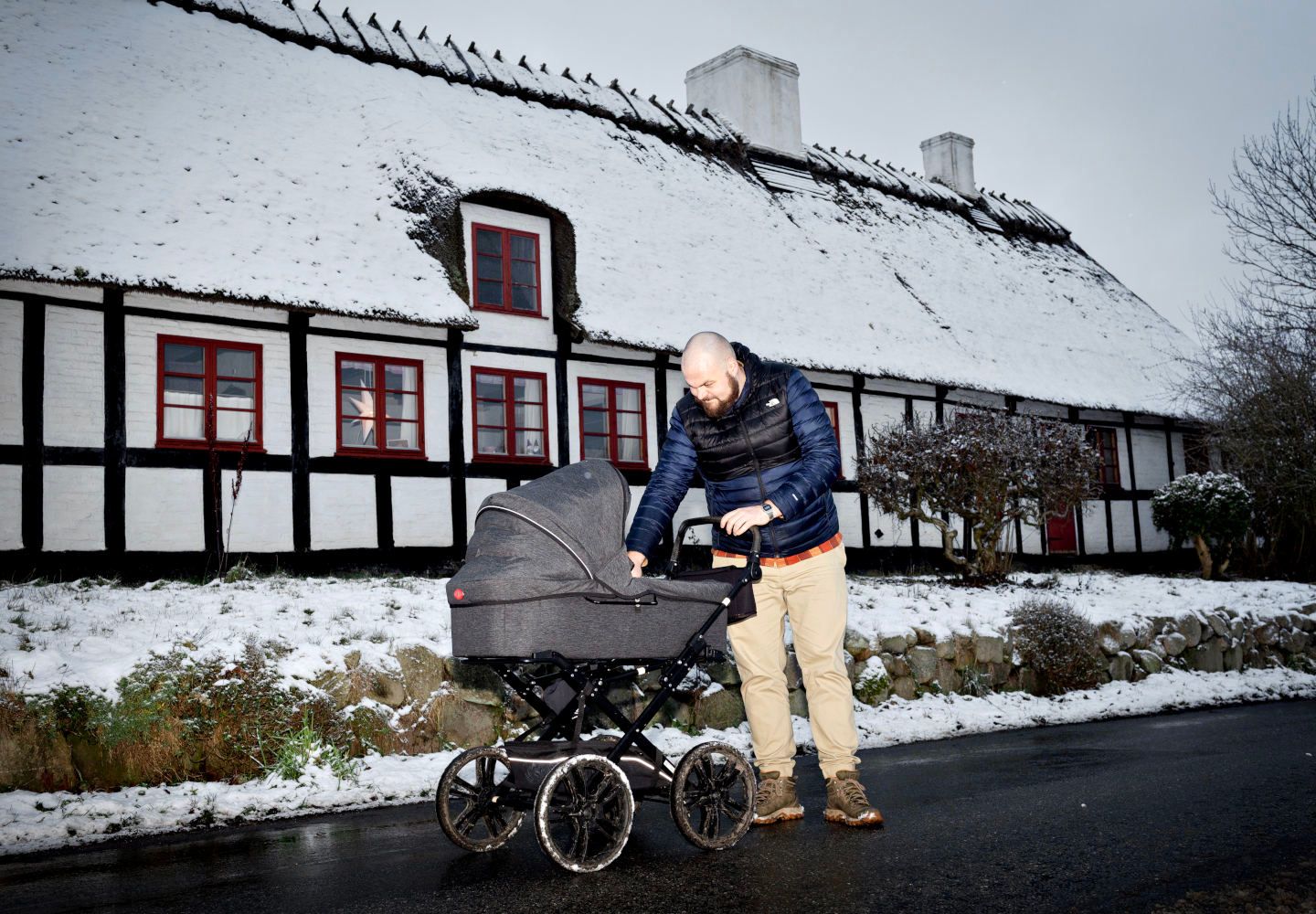 Jens Peter Hohnen står i vintertøj med en barnevogn foran et sneklædt bindingsværkshus