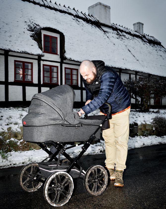 Jens Peter Hohnen står i vintertøj med en barnevogn foran et sneklædt bindingsværkshus.