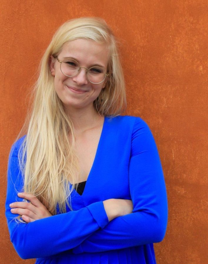 Portrætfoto af Maja Friis, smilende foran orange mur