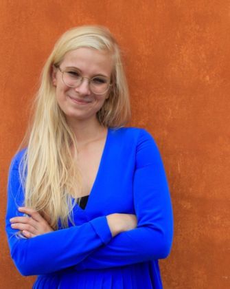 Portrætfoto af Maja Friis, smilende foran orange mur