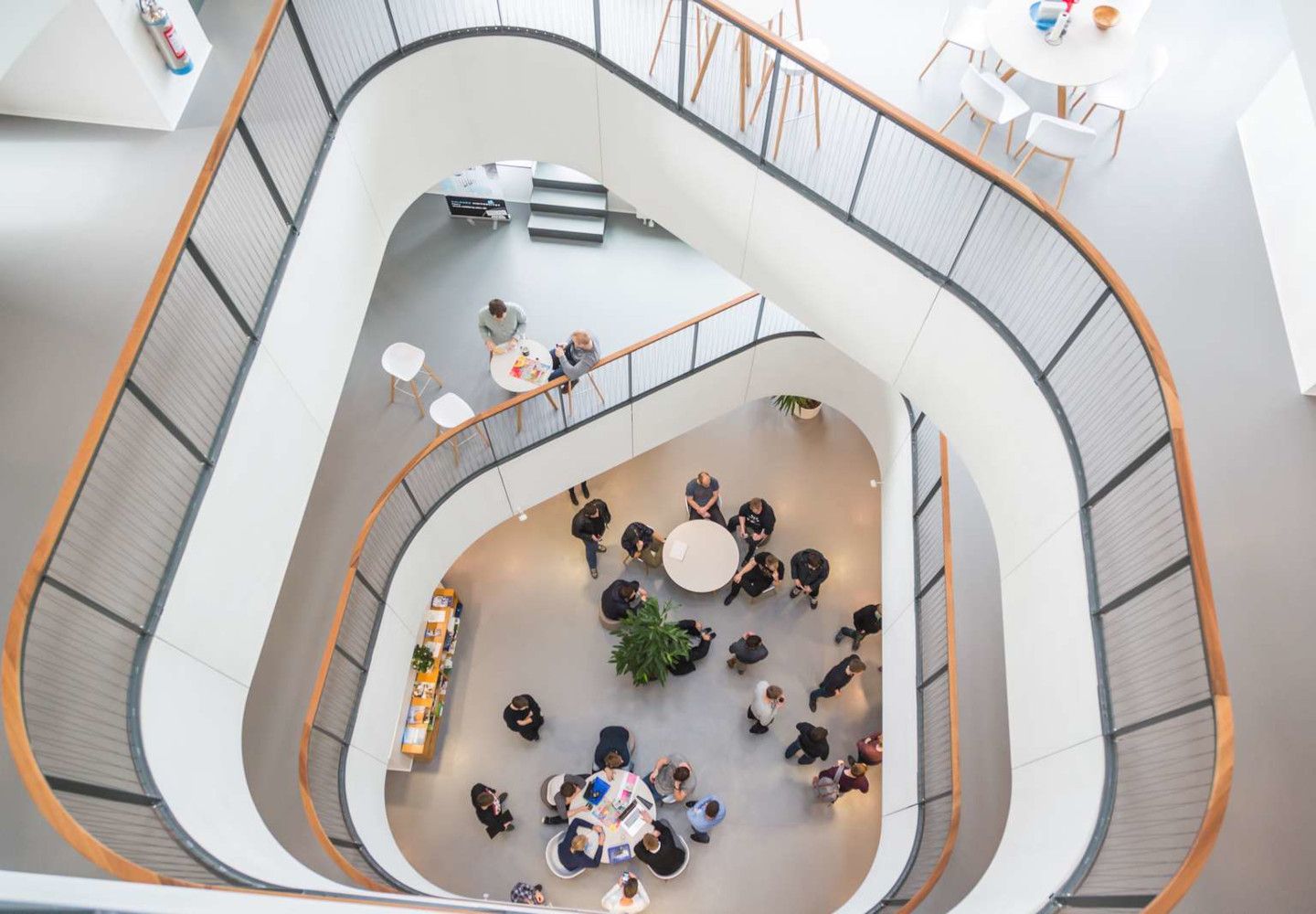 Foto fra Aalborg Universitets afdeling i Esbjerg, hvor man fra en etage højere oppe kan se grupper af studerende arbejde ved runde borde.