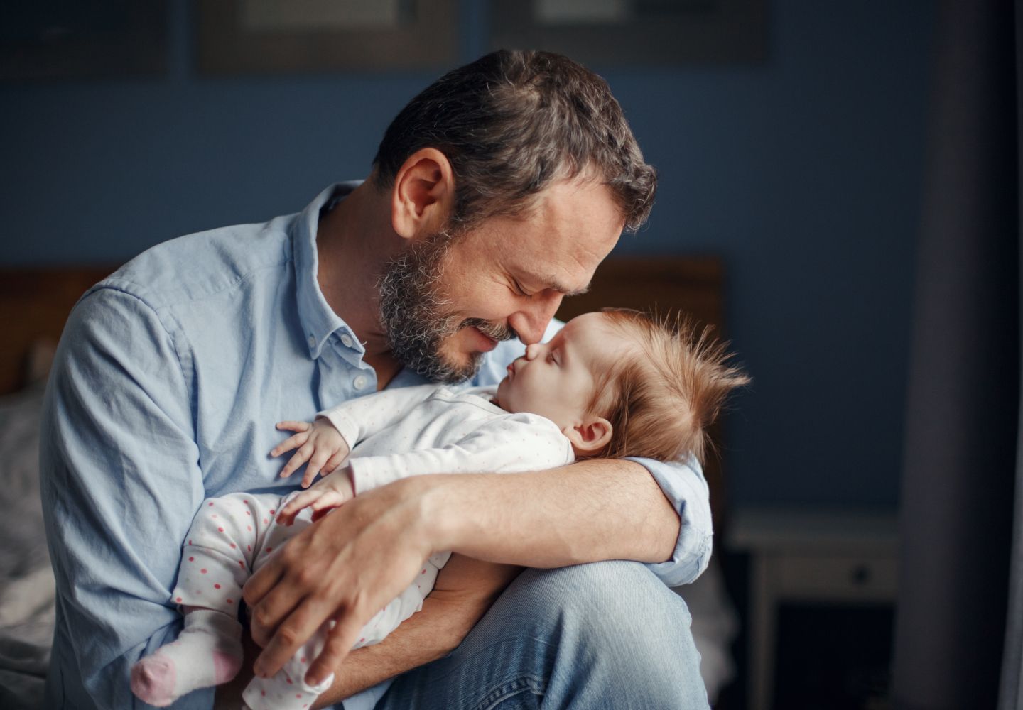 Foto af en smilende far, der sidder med en sovende baby i armene