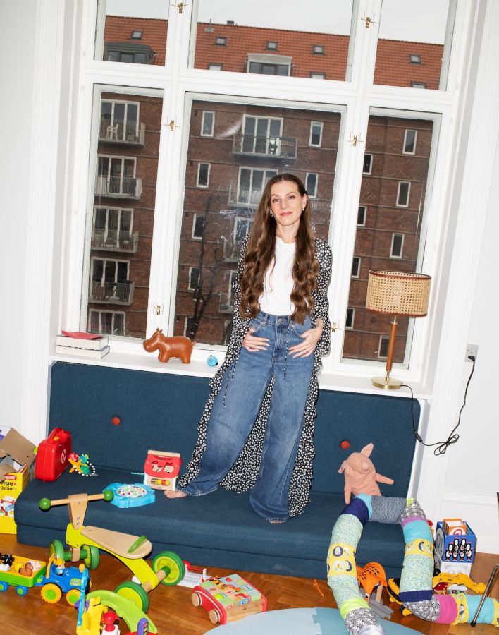 Foto af Isabella Hindkjær stående i en sofa ved et gulv fyldt med legetøj