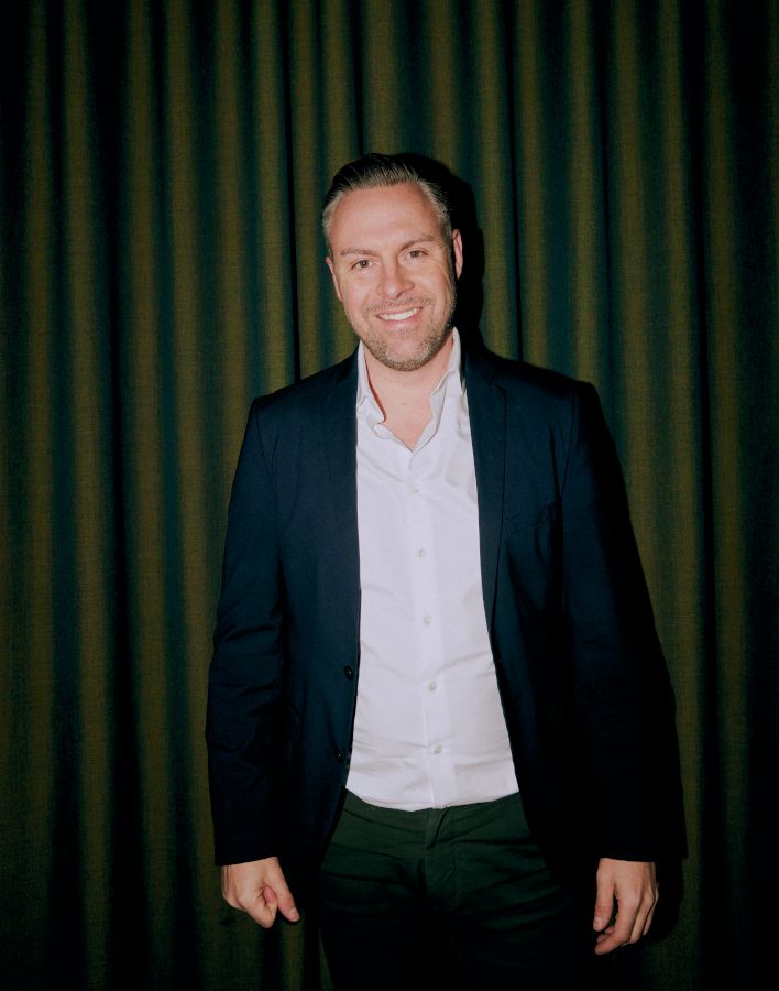 Portrætfoto af Kasper Heumann Kristensen, smilende foran et grønt gardin