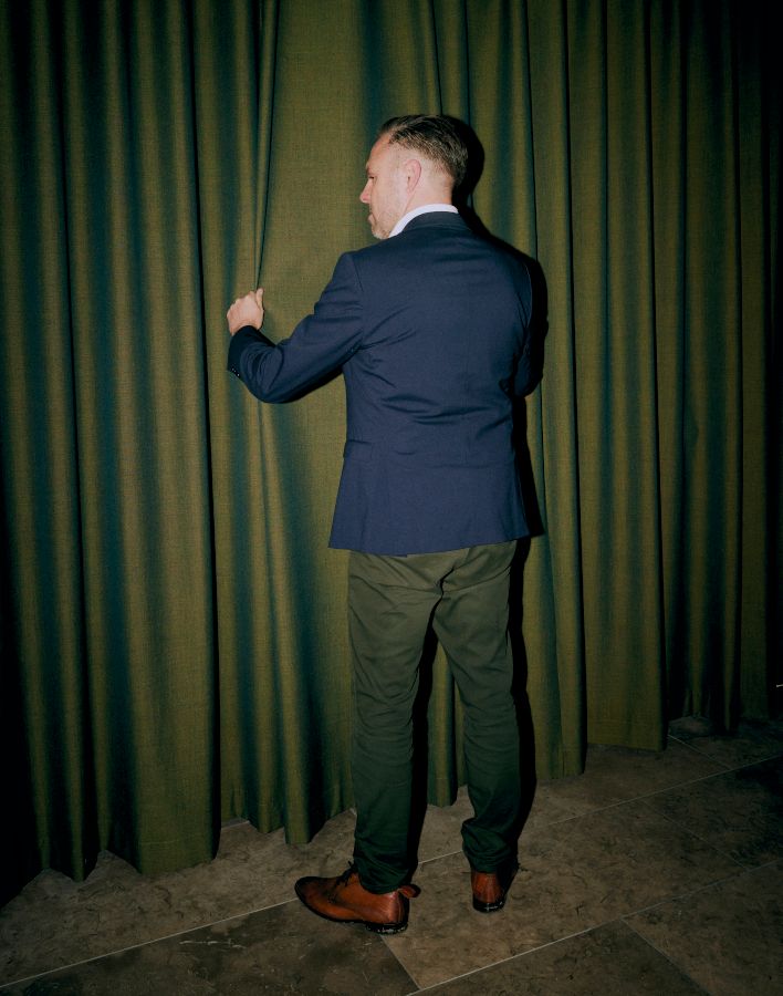 Portrætfoto af Kasper Heumann Kristensen, stående og i færd med at tilrette et grønt gardin