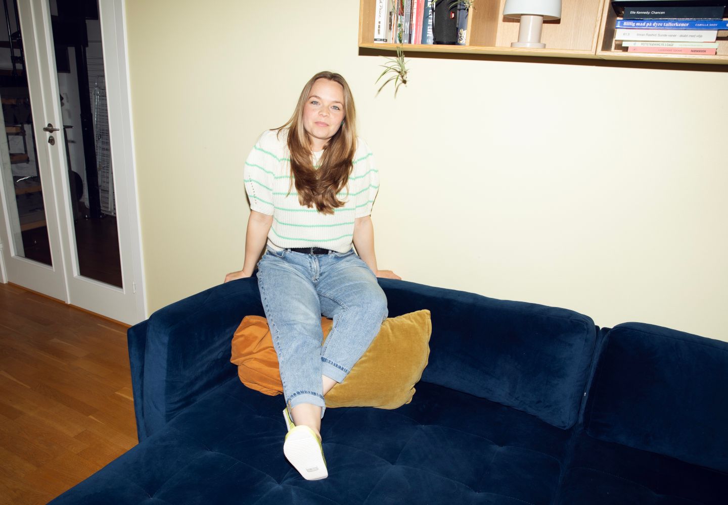 Foto af Stella Stegger, der smilende sidder på ryglænet af en stor mørkeblå sofa