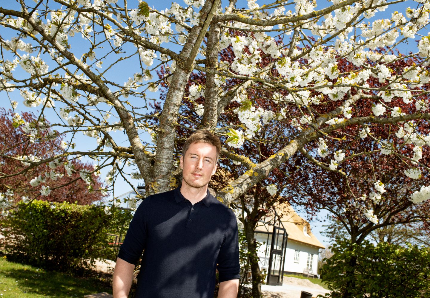 Foto af Jacob Mark foran et blomstrende træ ved den gård, han for nylig har købt