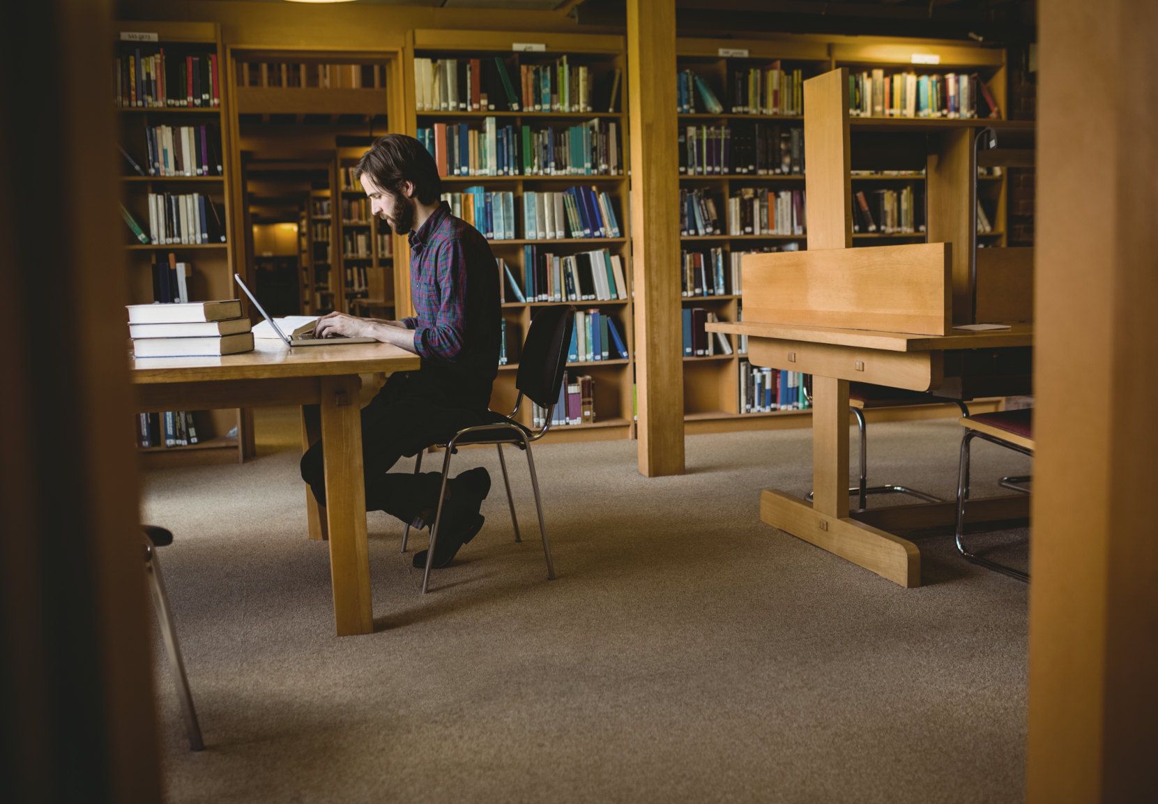 Foto af studerende, der sidder på et bibliotek og skriver på en laptop